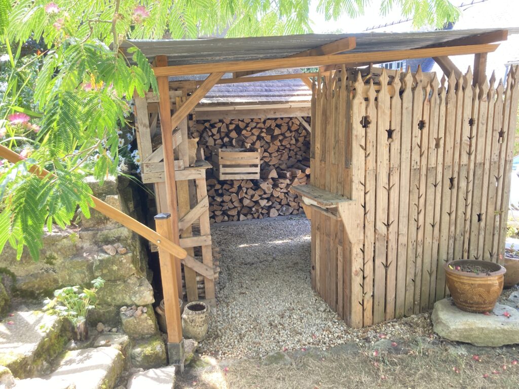 Petit abri à bois réalisé en réemploi avec bois de palettes et matériaux récupérés